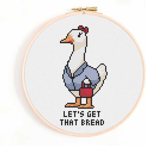 May include: A cross-stitch embroidery hoop featuring a pixelated goose wearing a blue jacket and holding a red purse. The text "LET'S GET THAT BREAD" is below the goose, all on a white background.