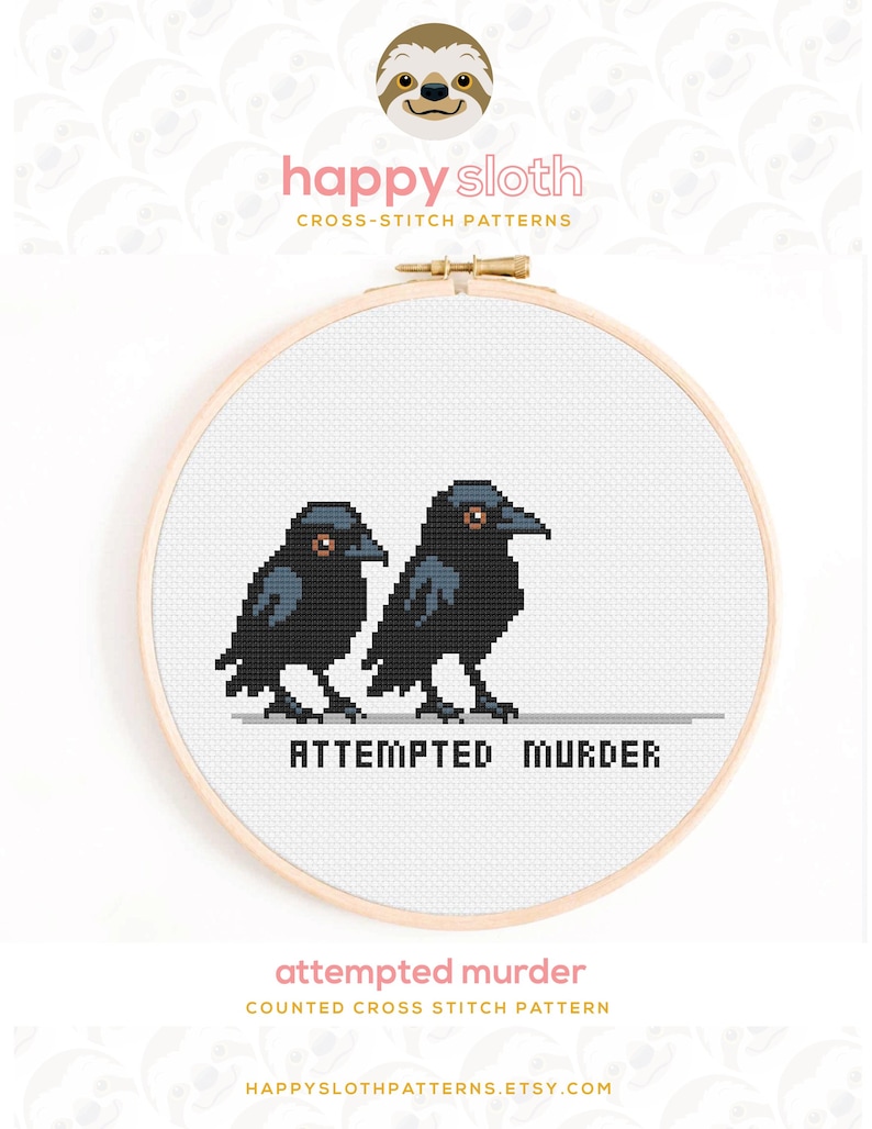 Puede incluir: Patr&oacute;n de punto de cruz con dos cuervos negros con ojos naranjas, uno al lado del otro. La frase "ATTEMPTED MURDER" est&aacute; bordada debajo de las aves. El dise&ntilde;o est&aacute; en un bastidor de bordado de madera.
