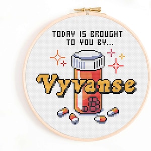 Może przedstawiać: Haft krzyżykowy w drewnianym tamborku z pikselowym wzorem. Tekst brzmi "TODAY IS BROUGHT TO YOU BY... Vyvanse" z ilustracją butelki z pigułkami i pigułkami. Projekt zawiera kolory pomarańczowy, ż&oacute;łty, biały i czerwony.