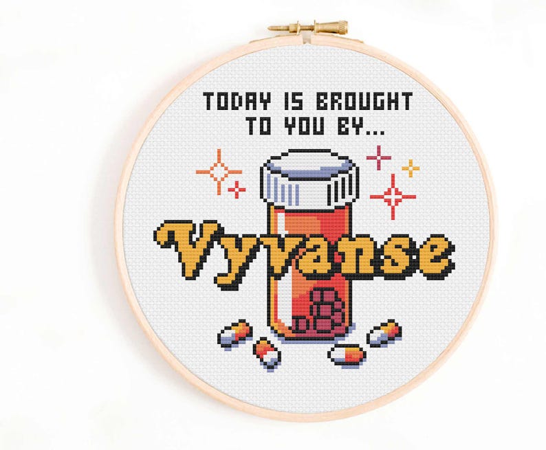 Może przedstawiać: Haft krzyżykowy w drewnianym tamborku z pikselowym wzorem. Tekst brzmi "TODAY IS BROUGHT TO YOU BY... Vyvanse" z ilustracją butelki z pigułkami i pigułkami. Projekt zawiera kolory pomarańczowy, ż&oacute;łty, biały i czerwony.