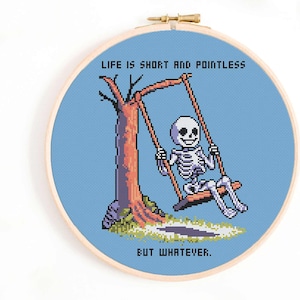 May include: Cross-stitch hoop art featuring a pixelated skeleton on a swing set. The skeleton is smiling, with a tree and the text "LIFE IS SHORT AND POINTLESS BUT WHATEVER." The background is light blue, and the hoop is wooden.