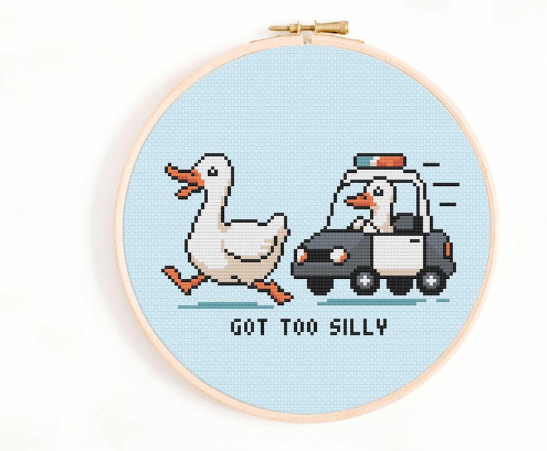May include: A cross-stitch hoop featuring a pixelated design of a white duck running from a police car driven by a duck. The text "GOT TOO SILLY" is below the car. The background is light blue.