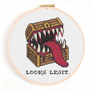 May include: Cross-stitch embroidery in a wooden hoop features a pixelated treasure chest with a large mouth full of teeth and a long red tongue. The text "LOOKS LEGIT." is below the chest.