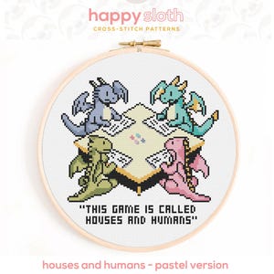 May include: A cross-stitch design in a wooden hoop, depicting four dragons in pastel shades playing a game. The text reads "THIS GAME IS CALLED HOUSES AND HUMANS". The design is labelled "houses and humans - pastel version".