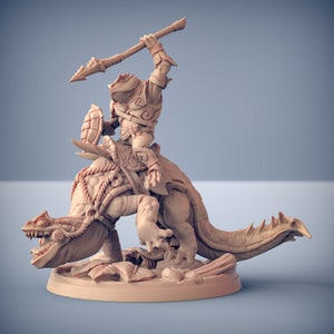 May include: A miniature figurine of a lizard-like creature with a rider. The rider is a humanoid figure with a spear and a shield. The figurine is painted in a light brown color.