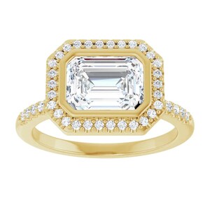 May include: A gold engagement ring with a large emerald-cut diamond center stone surrounded by a halo of smaller diamonds. The band is also set with smaller diamonds.