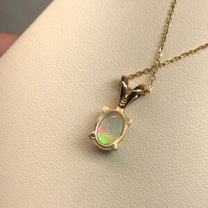 May include: A gold chain necklace with a pendant featuring a white opal gemstone set in a gold oval frame.