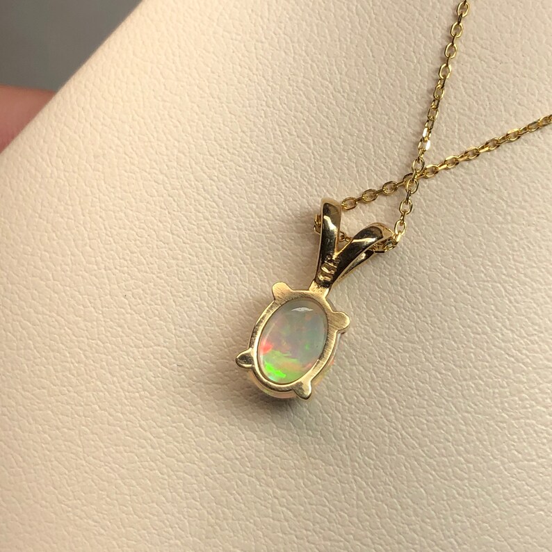 May include: A gold chain necklace with a pendant featuring a white opal gemstone set in a gold oval frame.