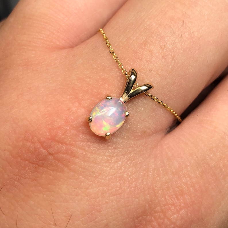 May include: A delicate gold chain necklace with a pendant featuring a white opal gemstone.