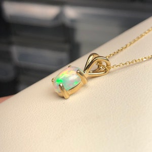 May include: A gold pendant necklace featuring a white opal gemstone. The opal displays a rainbow iridescent sheen.