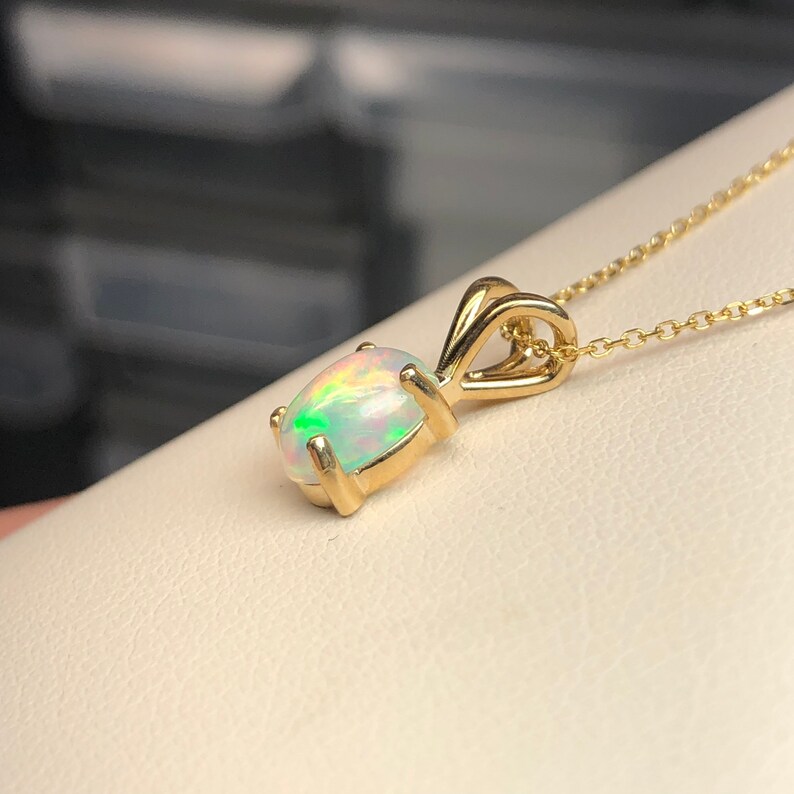 May include: A gold pendant necklace featuring a white opal gemstone. The opal displays a rainbow iridescent sheen.