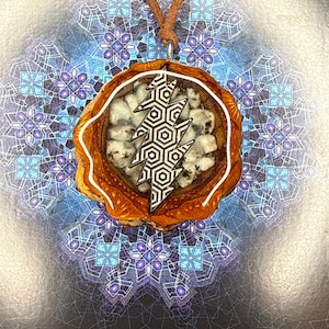 Puede incluir: Un collar con colgante con un marco marrón con efecto de madera y un borde blanco. El colgante presenta un diseño de rayo negro y blanco. El collar tiene un cordón de cuero marrón.