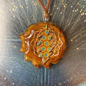 Puede incluir: Un collar con colgante que presenta un colgante marrón de forma orgánica con un diseño de rayo colorido. El rayo está hecho de varias formas geométricas en un arcoíris de colores. El collar tiene un cordón marrón.