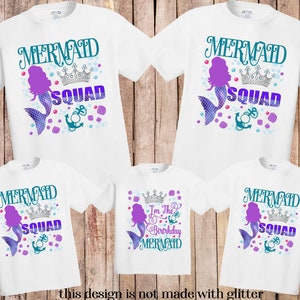 K&ouml;nnte beinhalten: Wei&szlig;e T-Shirts mit einem Meerjungfrauen-Design. Die Shirts zeigen die Worte "MERMAID SQUAD" in T&uuml;rkis und Lila, eine Meerjungfrauen-Illustration, eine Krone und einen Anker. Ein Shirt tr&auml;gt die Aufschrift "I'm the Birthday Mermaid". Der Text "this design is not made with glitter" steht unten.