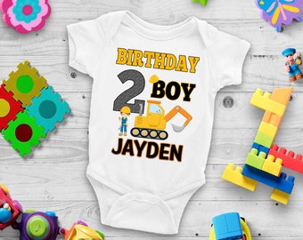 May include: White bodysuit with a yellow, black, and gray construction vehicle graphic. The text "Birthday Boy" and the number "2" are in black and yellow. The name "Jayden" is in black and yellow.