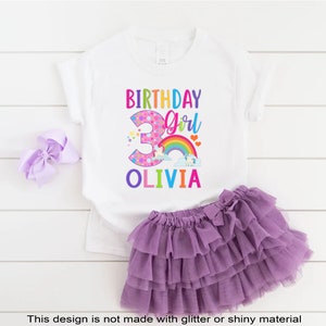 May include: White t-shirt with a colorful birthday girl design featuring a unicorn, rainbow, and the number 3. The text "Birthday Girl" and "Olivia" are also included.