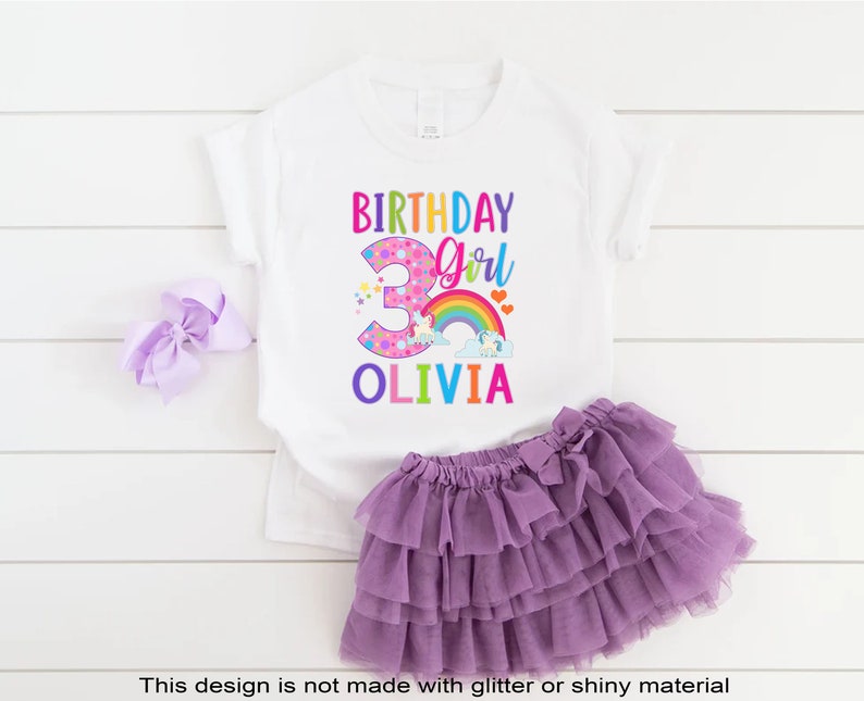 May include: White t-shirt with a colorful birthday girl design featuring a unicorn, rainbow, and the number 3. The text "Birthday Girl" and "Olivia" are also included.