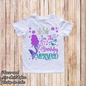 K&ouml;nnte beinhalten: Wei&szlig;es T-Shirt mit einer lila Meerjungfrau, einer silbernen Krone und dem Text "I'm The Birthday Mermaid" in T&uuml;rkis und Lila. Das Design umfasst Muscheln und Blasen.