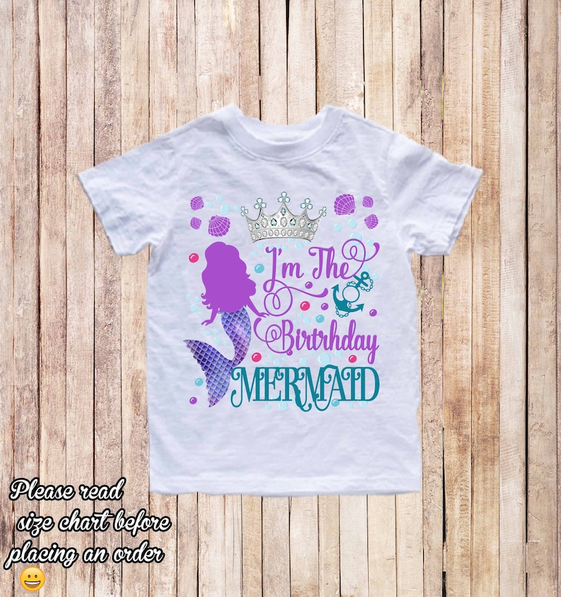 K&ouml;nnte beinhalten: Wei&szlig;es T-Shirt mit einer lila Meerjungfrau, einer silbernen Krone und dem Text "I'm The Birthday Mermaid" in T&uuml;rkis und Lila. Das Design umfasst Muscheln und Blasen.