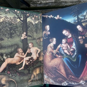 May include: Open book with two Renaissance-style paintings. One depicts Adam and Eve in a garden with animals. The other shows the Virgin Mary with baby Jesus and other figures, all under a dark blue sky.