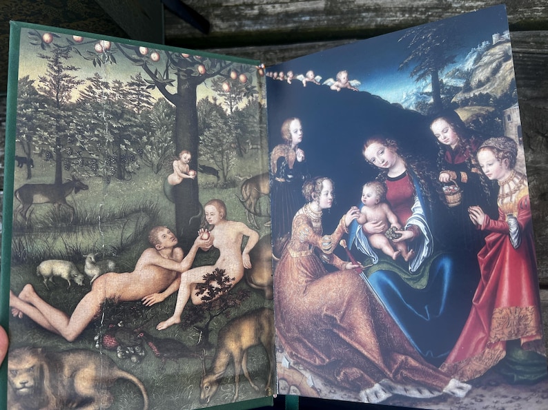 May include: Open book with two Renaissance-style paintings. One depicts Adam and Eve in a garden with animals. The other shows the Virgin Mary with baby Jesus and other figures, all under a dark blue sky.