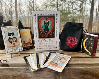 Könnte beinhalten: Ein Cat Folk Tarot-Deck mit 78 Karten und einem 161-seitigen Handbuch. Die Schachtel zeigt eine schwarze Katze mit einem roten Herzen und floralen Designs. Das Deck wird mit einem schwarzen Samtbeutel mit einem roten Herzdesign geliefert.