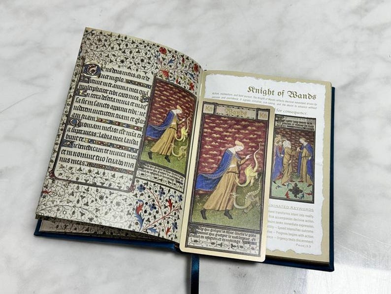 May include: An open book with illuminated manuscript-style pages featuring intricate floral borders and Latin text. A rectangular tarot card titled Knight of Wands, depicting a figure in a blue cloak and tan robe with a dragon, rests on the right page.