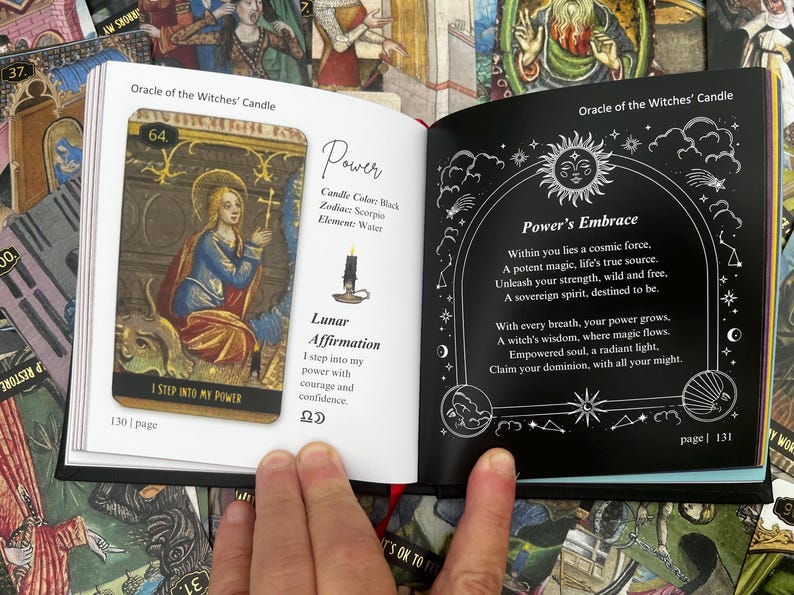 May include: An open book displaying tarot cards. One page features a card with a woman in blue and gold, the text "I STEP INTO MY POWER", and the number 64. The opposite page has the text "Power's Embrace" with a sun and moon design.
