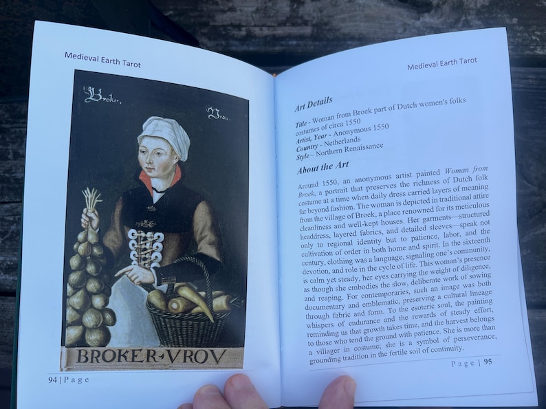 May include: An open book displaying a tarot card illustration from the Medieval Earth Tarot deck. The card features a portrait of a woman in Dutch folk costume from circa 1550, holding vegetables and a basket.