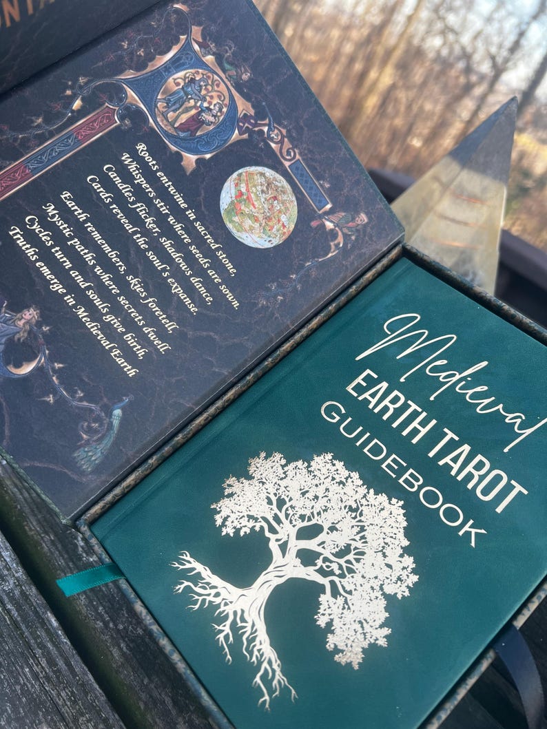 May include: A Medieval Earth Tarot Guidebook with a teal cover and gold lettering. The cover features a detailed white tree illustration. The open box reveals text and illustrations, including the phrases "Roots entwine in sacred stone" and "Medieval Earth".