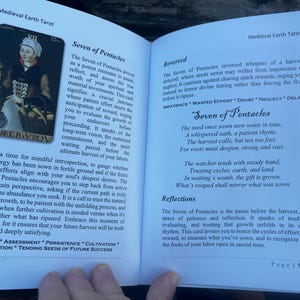 May include: Open book with a Medieval Earth Tarot spread. The left page features the "Seven of Pentacles" card with an illustration of a person and text. The right page has text about the card's reversed meaning.