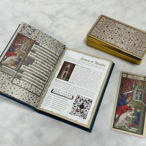 May include: An open book with medieval-style illustrations and text, a deck of tarot cards with gold edges, and a single Seven of Wands tarot card. The book pages feature intricate floral borders, Latin text, and a detailed description of the card.