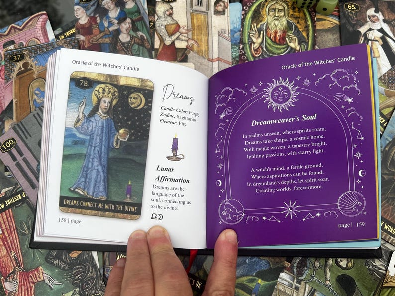 May include: An open book displaying two pages from an oracle card deck. One page features a card with a figure in blue robes, the text "Dreams Connect Me With The Divine", and the number 78. The opposite page has purple text and illustrations.