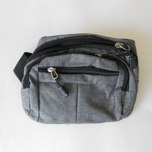 May include: A gray fanny pack with black zipper accents and a black strap. The pack has multiple zippered compartments.