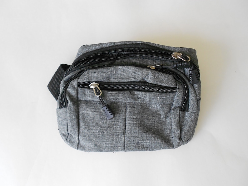May include: A gray fanny pack with black zipper accents and a black strap. The pack has multiple zippered compartments.
