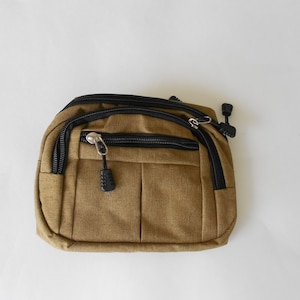 May include: A small brown canvas fanny pack with black zipper accents and a black zipper pull.