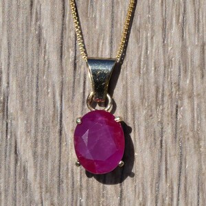 May include: A gold chain necklace with a pendant featuring a large oval-shaped ruby gemstone.