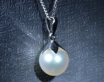 Puede incluir: Un collar con un colgante de perla blanca y una cadena de plata. La perla es redonda y tiene un ligero brillo iridiscente.