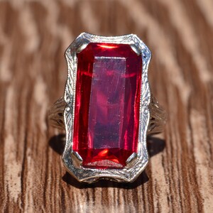 May include: A silver ring with a large, rectangular, red gemstone.