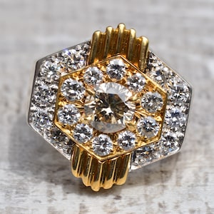 May include: A gold and silver ring featuring a large, round, brown diamond surrounded by smaller diamonds. The ring is set in a hexagonal shape.