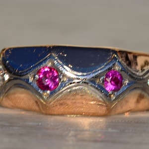 May include: A gold ring with two pink gemstones and small white gemstones set in a decorative design.