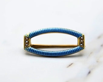May include: A blue enamel and gold oval brooch with a row of pearls on each side.
