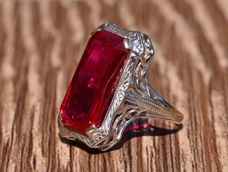 May include: A vintage ring featuring a large, rectangular, red gemstone set in a filigree design.