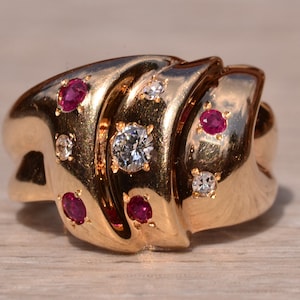 Può includere: Un anello d'oro con un design a spirale incastonato con rubini rossi e diamanti trasparenti.