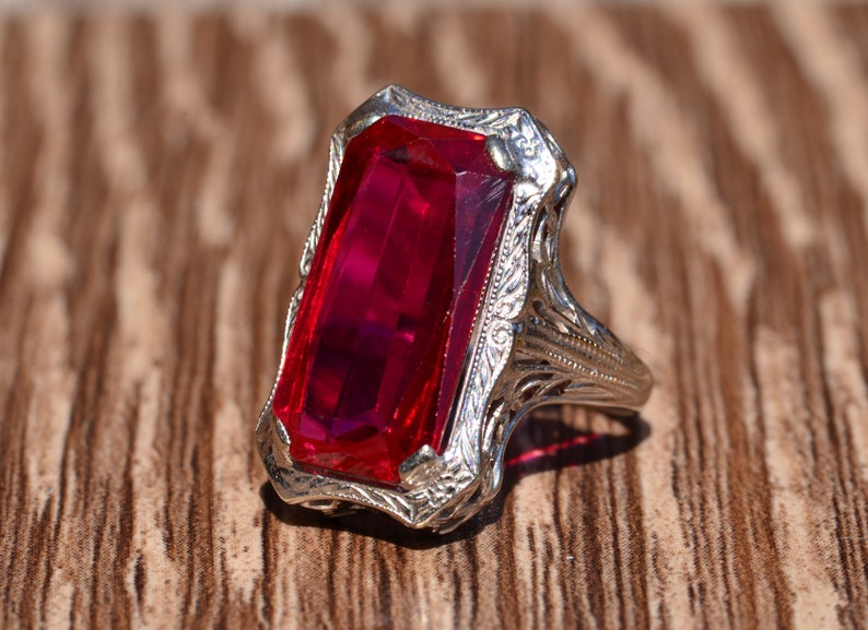 May include: A vintage ring featuring a large, rectangular, red gemstone set in a filigree silver band.