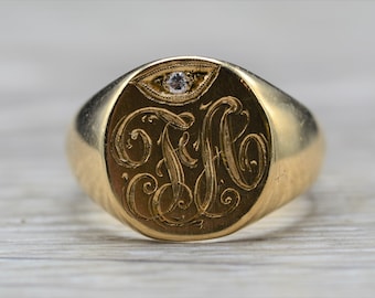 May include: A gold signet ring with a single diamond set in the top. The ring features an engraved monogram.