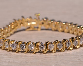 May include: A gold tennis bracelet with a row of clear round stones set in a wavy pattern.