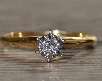 Könnte beinhalten: Ein Goldring mit einem einzelnen runden Diamanten, der in einer weißen Metallfassung sitzt.