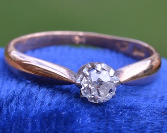 Puede incluir: Un delicado anillo de oro con un solo diamante redondo engastado en garras. El anillo tiene un diseño simple y elegante.