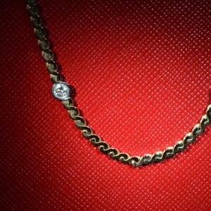 May include: A gold chain necklace with two small, clear gemstones. The necklace is on a red background.